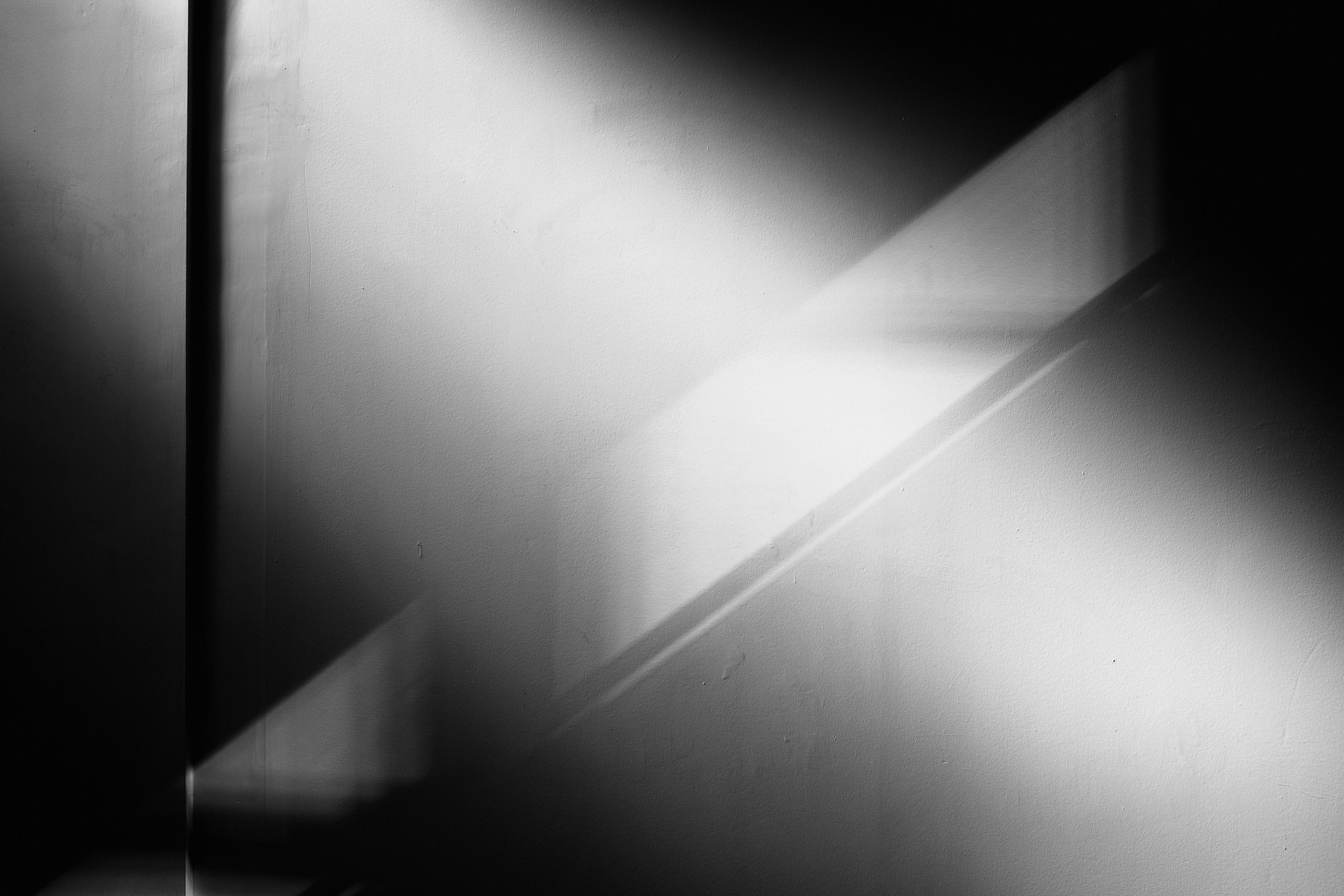 Black and white photograph of daylight falling through a window in a diagonal shaft across a dark wall
